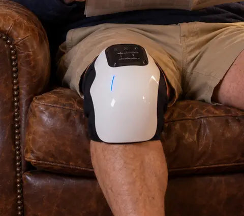 The knee massager on a man's knee in a leather armchair, the black wrap closed around the back of the knee